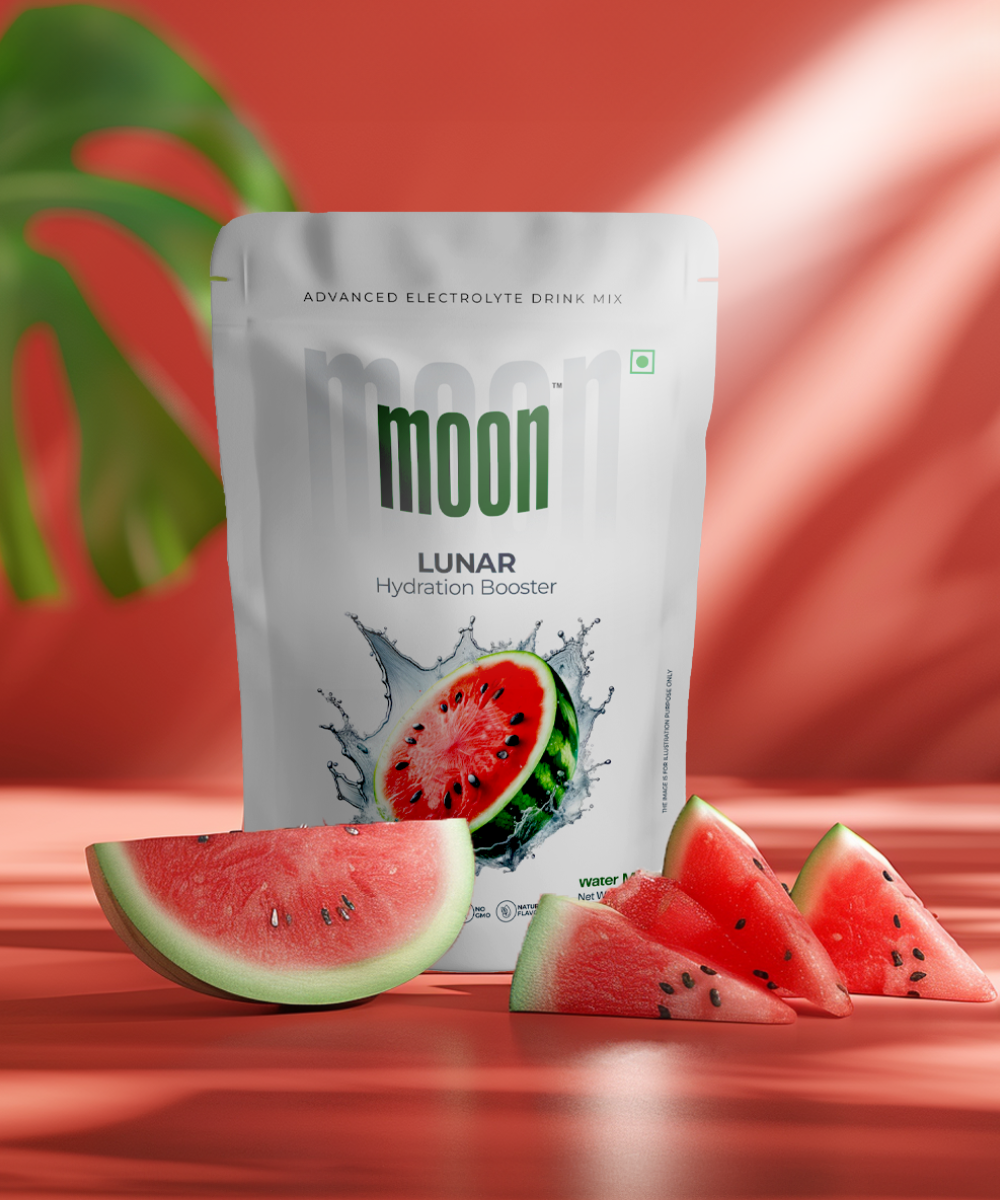 A package of "Moon Lunar Watermelon Hydration Booster" electrolyte drink mix by MOONFREEZE FOODS PRIVATE LIMITED is displayed on a table next to watermelon slices, with a plant leaf in the background.