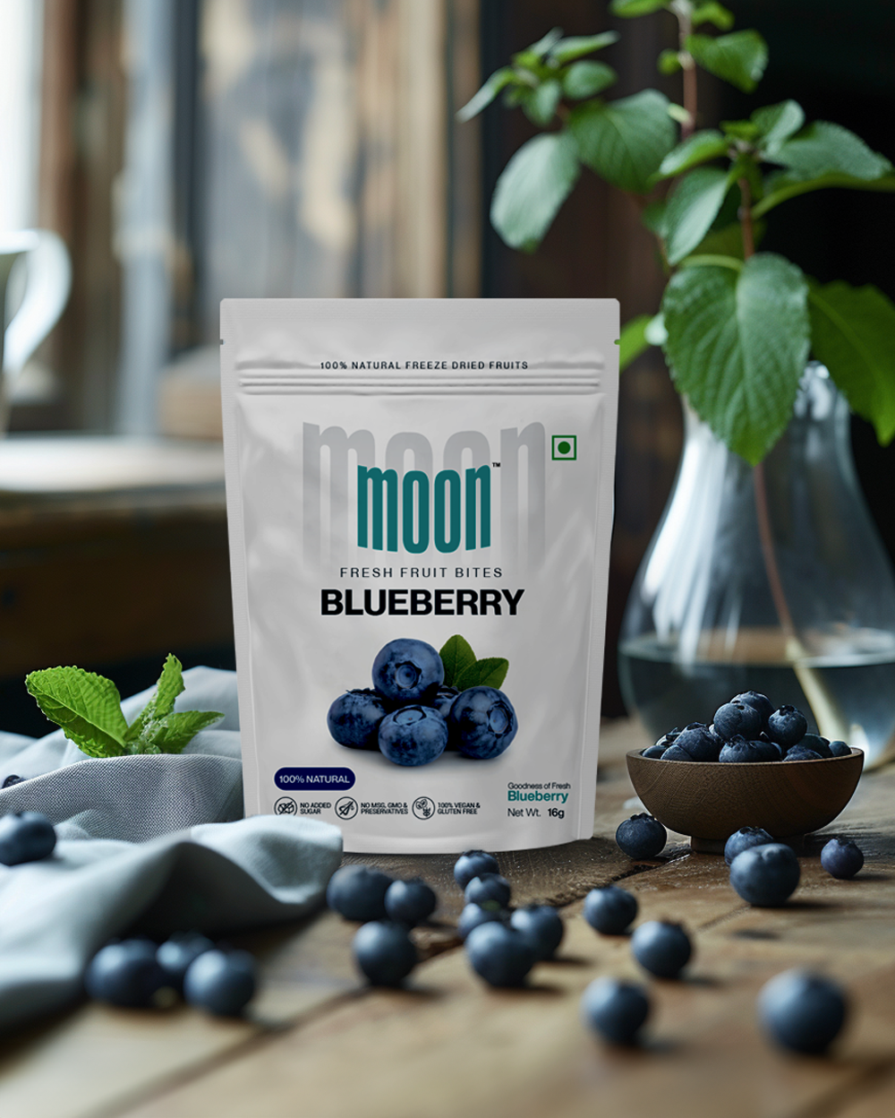Fresh Fruit Bites in Blueberry flavor, elegantly displayed on a wooden table with fresh blueberries and a vase of green leaves, emphasizing the natural and wholesome qualities of the product.