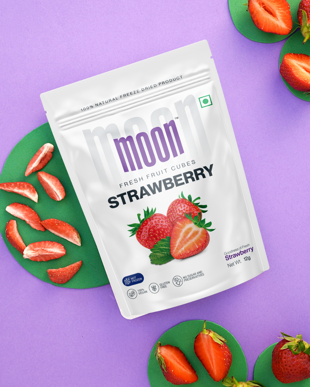 A package of nutritious snack Moon Freeze Dried Mango Cube + Strawberry on a purple background, surrounded by fresh strawberries and green coasters.