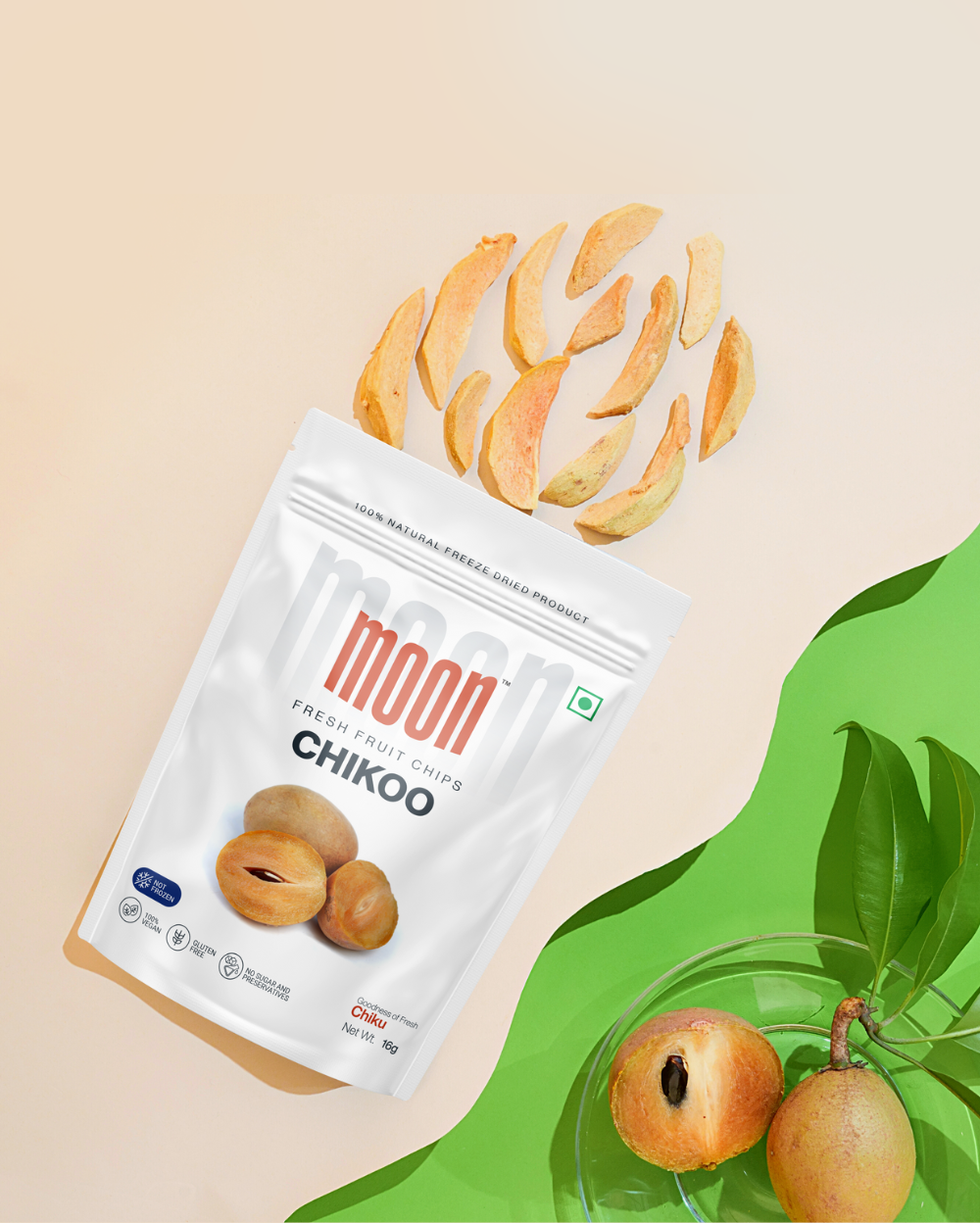 A packet of Moon Freeze Dried Chikoo + Kiwi slices with fresh chikoos and leaves on a beige background.