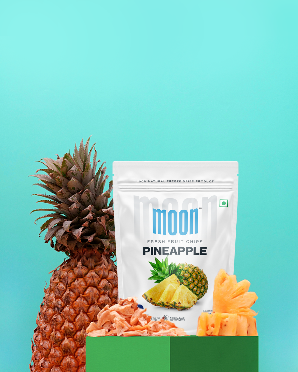 A pack of Moon Freeze Dried Chikoo + Pineapple fruit chips alongside a fresh pineapple on a durable two-tone background.