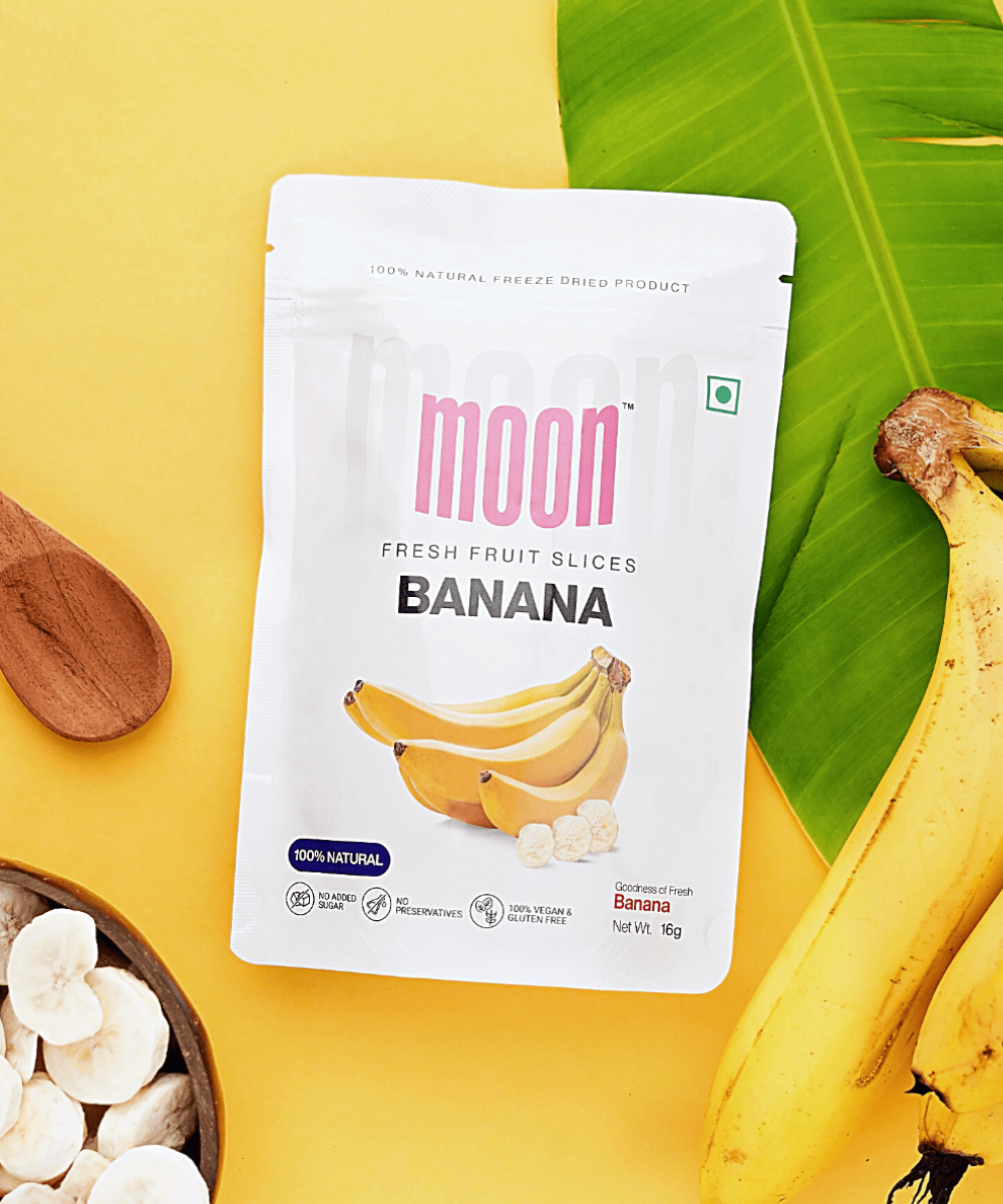 MOONFREEZE FOODS PRIVATE LIMITED's Packaged Moon Freeze Assorted Healthy Chips for Kids on a yellow background with fresh bananas and banana leaves, offered in assorted flavors.