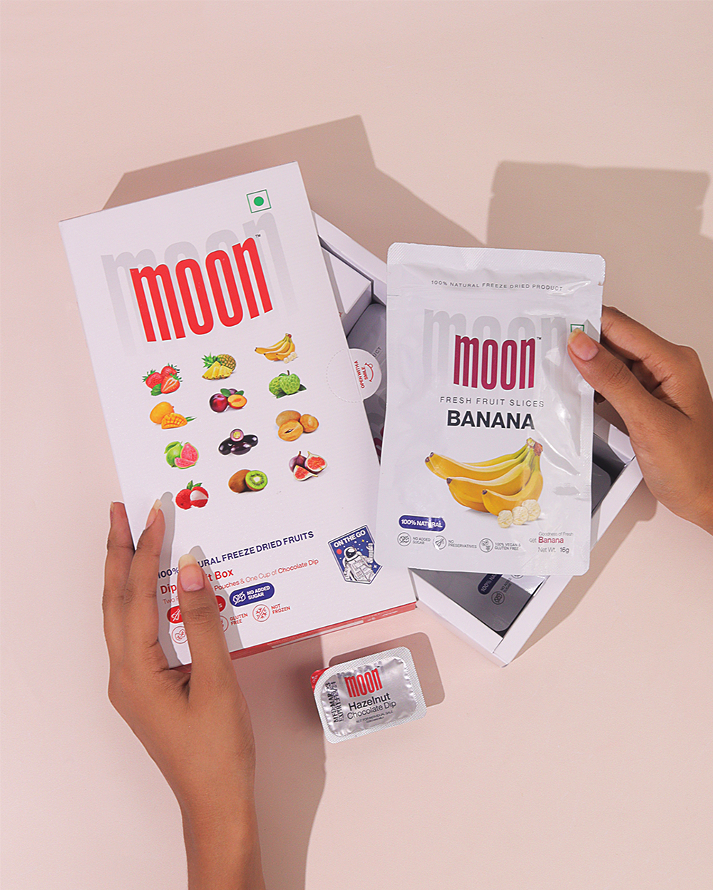A hand holding a box of Moon Freeze Dried Yellow Quarter moon fruit and bananas manufactured by MOONFREEZE FOODS PRIVATE LIMITED.