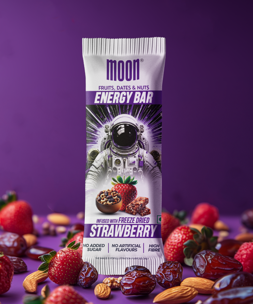 A single MOON Energy Bar - Strawberry by MOONFREEZE FOODS PRIVATE LIMITED is displayed amidst fresh strawberries, dates, almonds, and cacao nibs on a purple surface. The packaging showcases an astronaut design. Ideal as a meal replacement, it pairs wonderfully with freeze-dried mangoes for an extraordinary snack experience.