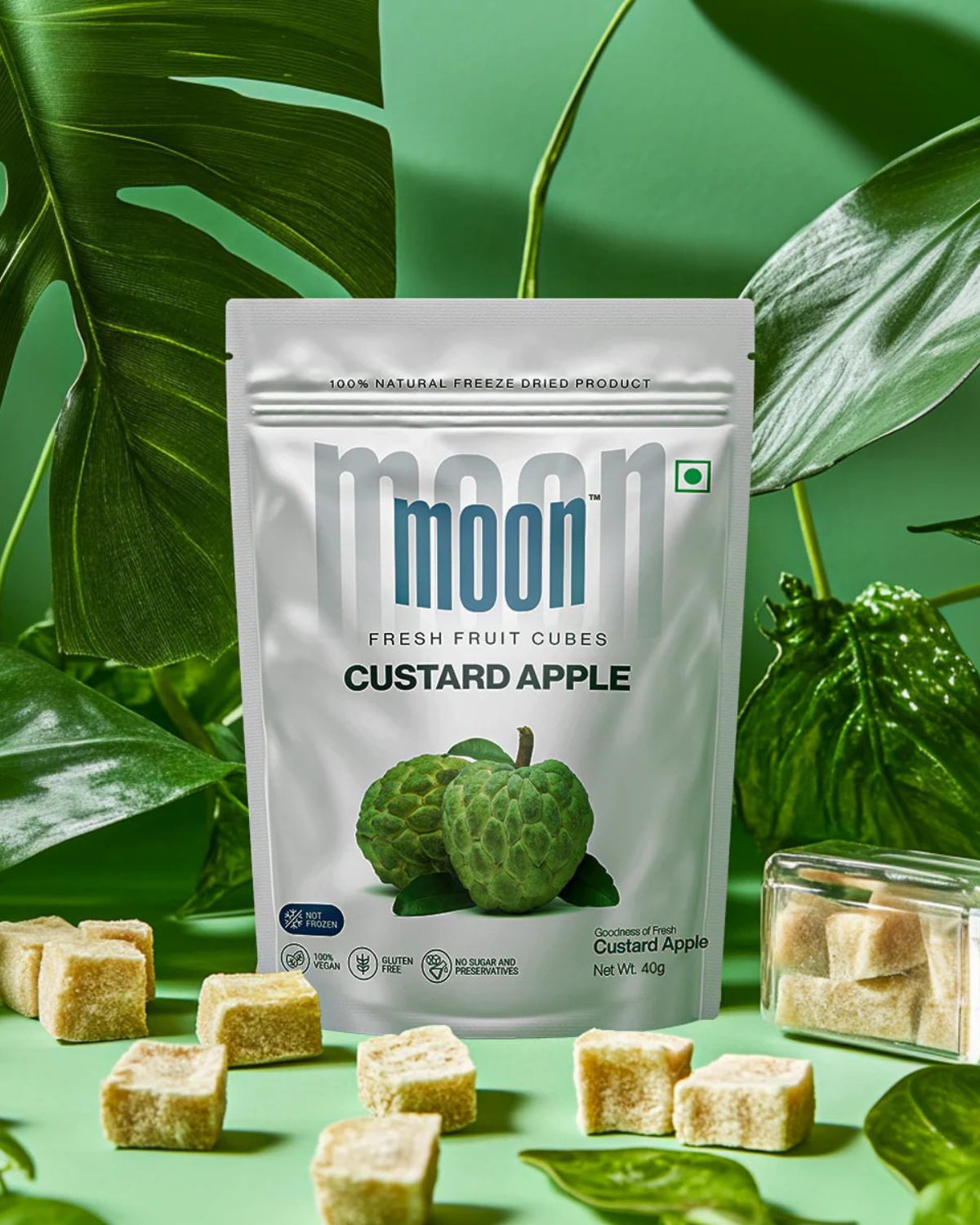 Moon Freeze Dried Custard Apple Cubes by Themoonstoreindia are shown upright with cubes and green leaves on a green background. Enjoy 100% natural goodness with no added sugar.