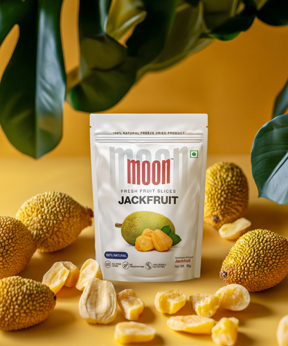 A pack of Themoonstoreindia's Moon Freeze Dried Jackfruit stands upright among fresh jackfruits and loose chips on a yellow surface, with green leaves behind—offering a 100% natural, healthy snack choice.