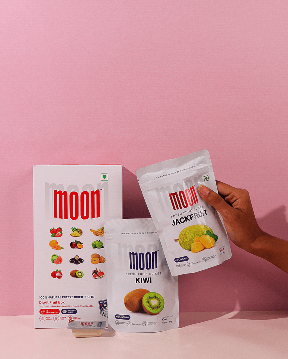 A person holding a bag of Moon Freeze Dried Fifth Quarter by MOONFREEZE FOODS PRIVATE LIMITED and a bag of kiwi.