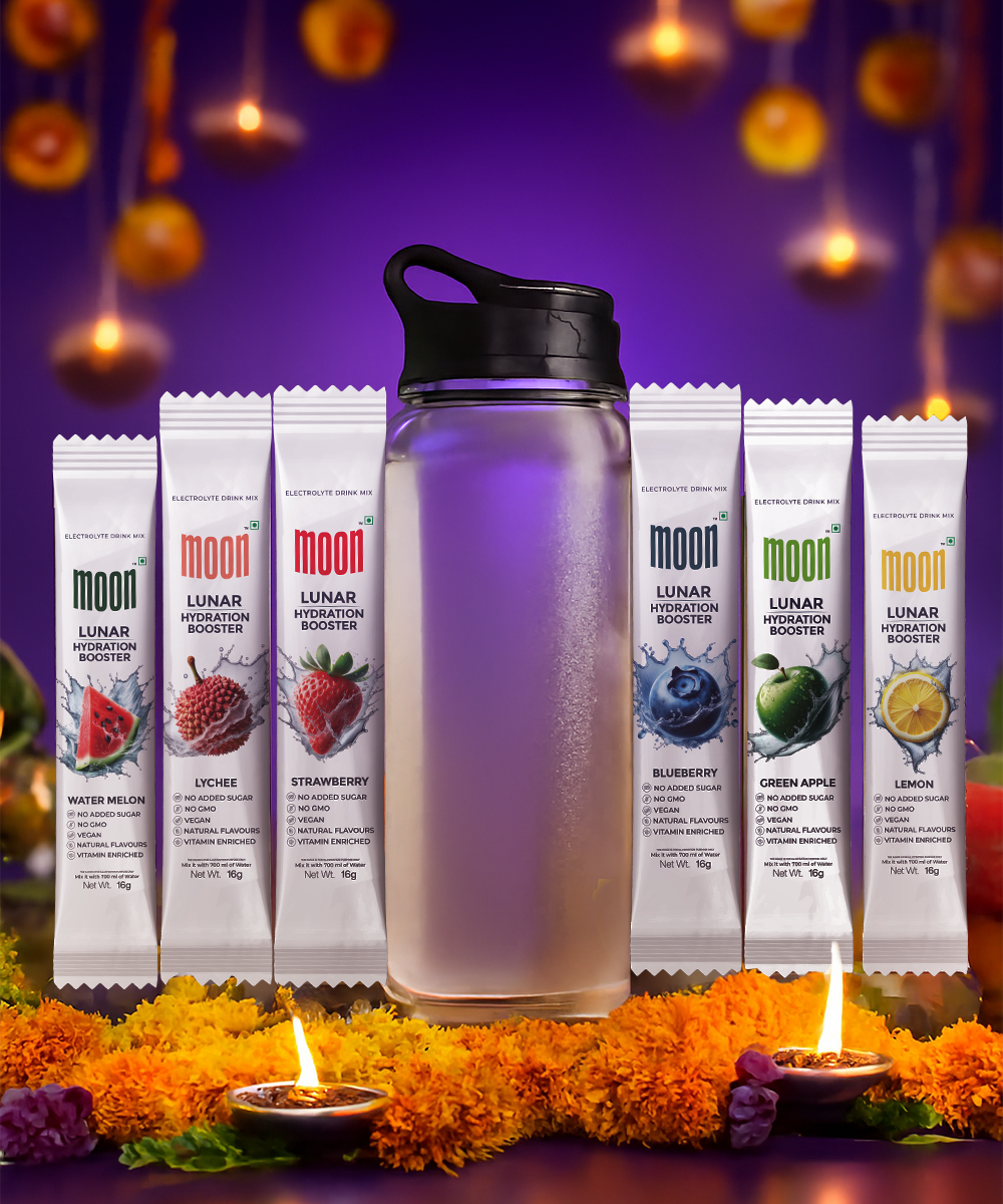 A MOONFREEZE FOODS PRIVATE LIMITED Lunar Hydration Booster - Variety Pack (With Bottle) is displayed with sachets and drink packs in assorted flavors, surrounded by marigold flowers, candles, and festive decorations in the background.