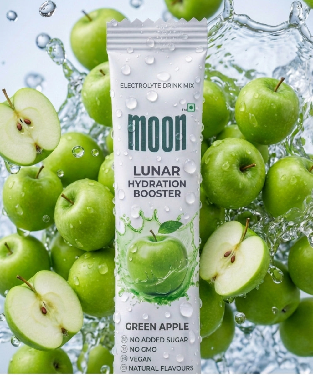 A Lunar Hydration Booster - Green Apple Flavour packet by MOONFREEZE FOODS PRIVATE LIMITED sits among fresh green apples and water splashes, showcasing its electrolytes and B-vitamin complex for superior hydration.