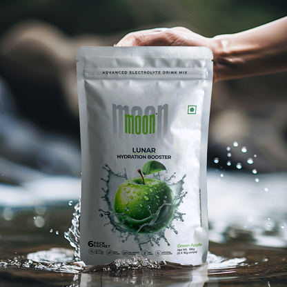 A hand holds a packet of "Lunar Hydration Booster - Green Apple | Electrolyte Drink Mix," an advanced electrolyte-rich drink mix from MOONFREEZE FOODS PRIVATE LIMITED. The packet displays an image of a green apple splashing into water.