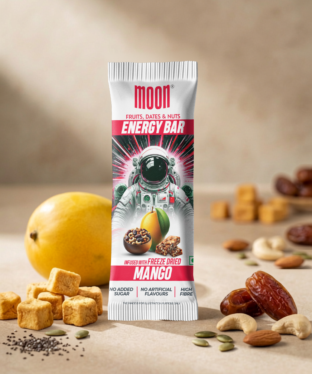 The MOON Energy Bar - Mango by MOONFREEZE FOODS PRIVATE LIMITED stands upright among dried fruits, nuts, and a whole mango—ideal as a delicious meal replacement or snack.