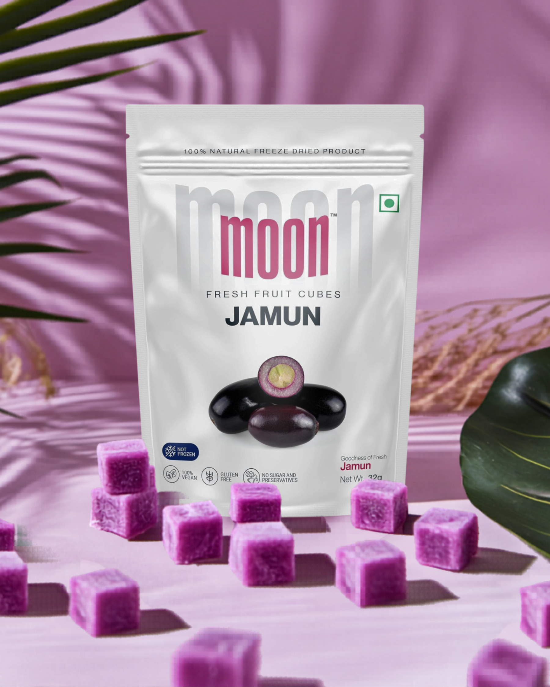 A package of Themoonstoreindia Moon Freeze Dried Jamun Cubes stands upright on a pink background, surrounded by purple fruit cubes and tropical leaves—the perfect natural remedy for sugar cravings.
