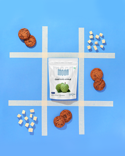 A bag of Moon Freeze Dried Custard Apple Cubes on a blue background with a tic-tac-toe board. (Brand: Themoonstoreindia)