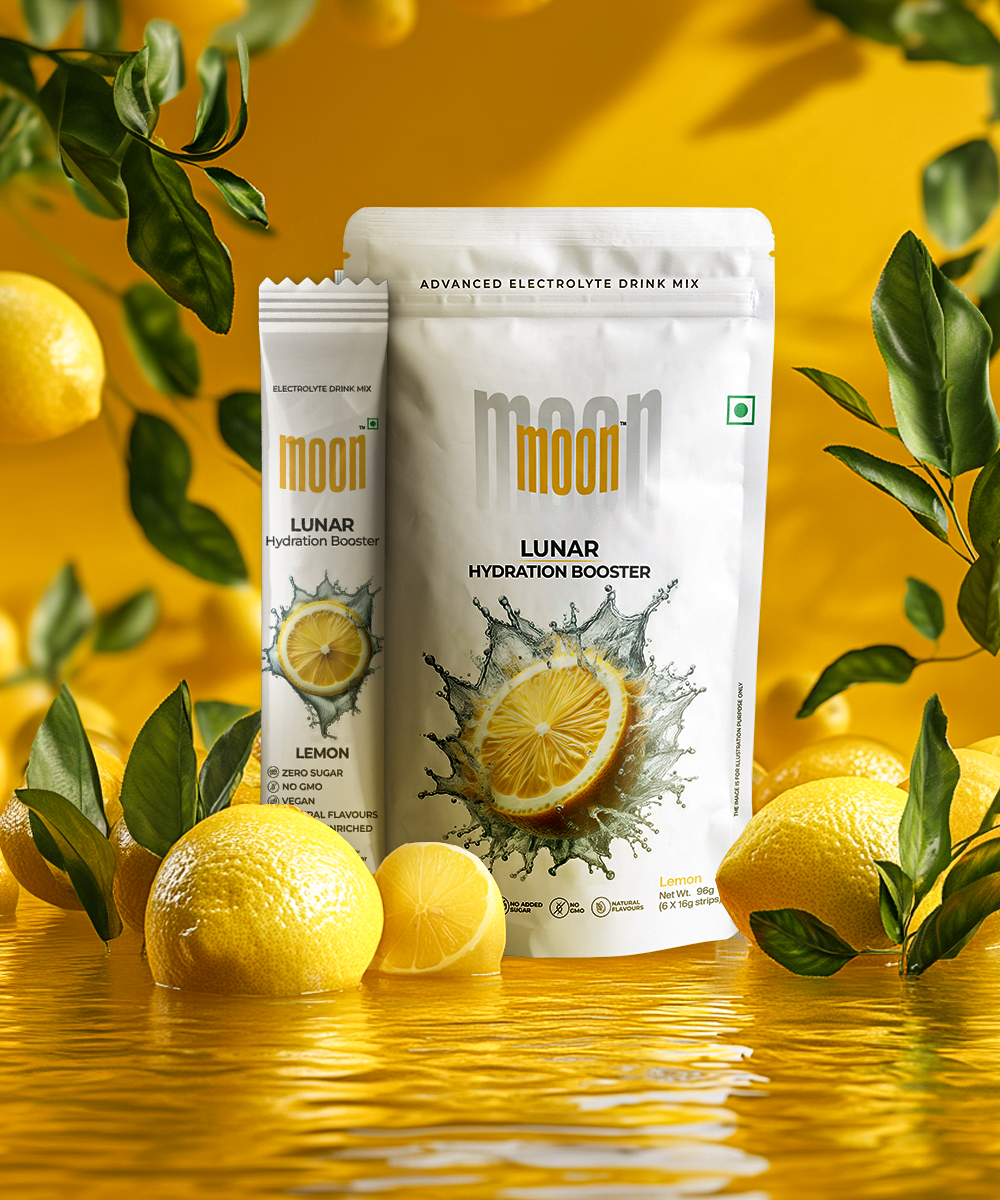 A packet and a tube of MOONFREEZE FOODS PRIVATE LIMITED's Lunar Hydration Booster - Lemon | Electrolyte Drink Mix in lemon flavor are surrounded by fresh lemons and lemon leaves against a yellow background with a reflective surface.