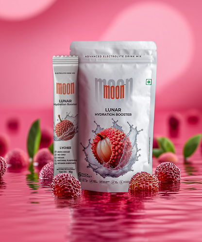 A packet and stick of MOONFREEZE FOODS PRIVATE LIMITED's Lunar Hydration Booster - Lychee Electrolyte Drink Mix, displayed with lychees and green leaves in the background against a pink backdrop and reflective surface. This delicious drink mix is perfect for staying hydrated throughout your adventures.