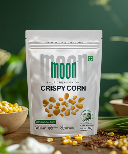 A package of "Freeze Dried Crispy Corn Sour Cream & Onion" from MOONFREEZE FOODS PRIVATE LIMITED is displayed. The bag features scattered corn kernels and a green natural product label, highlighting its plant-based ingredients, with the net weight noted at the bottom.