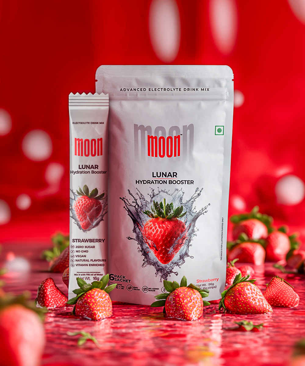 Two packages of "Lunar Hydration Booster - Strawberry," an electrolyte drink mix from MOONFREEZE FOODS PRIVATE LIMITED, are displayed: one large resealable pouch and one single-serving stick pack, surrounded by fresh strawberries on a red surface. Enjoy this sugar-free hydration boost for a refreshing experience.