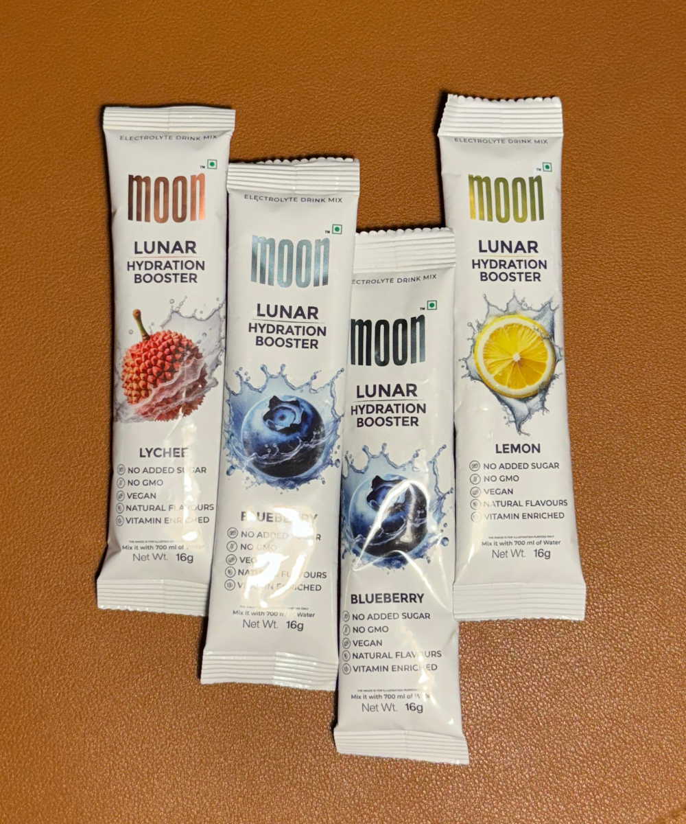 A Festive Feast Hamper from MOONFREEZE FOODS PRIVATE LIMITED, featuring four packets of Moon Lunar Hydration Booster drink mix in lychee, blueberry, and lemon flavors, sits alongside the Lunar Sticks on a brown surface.