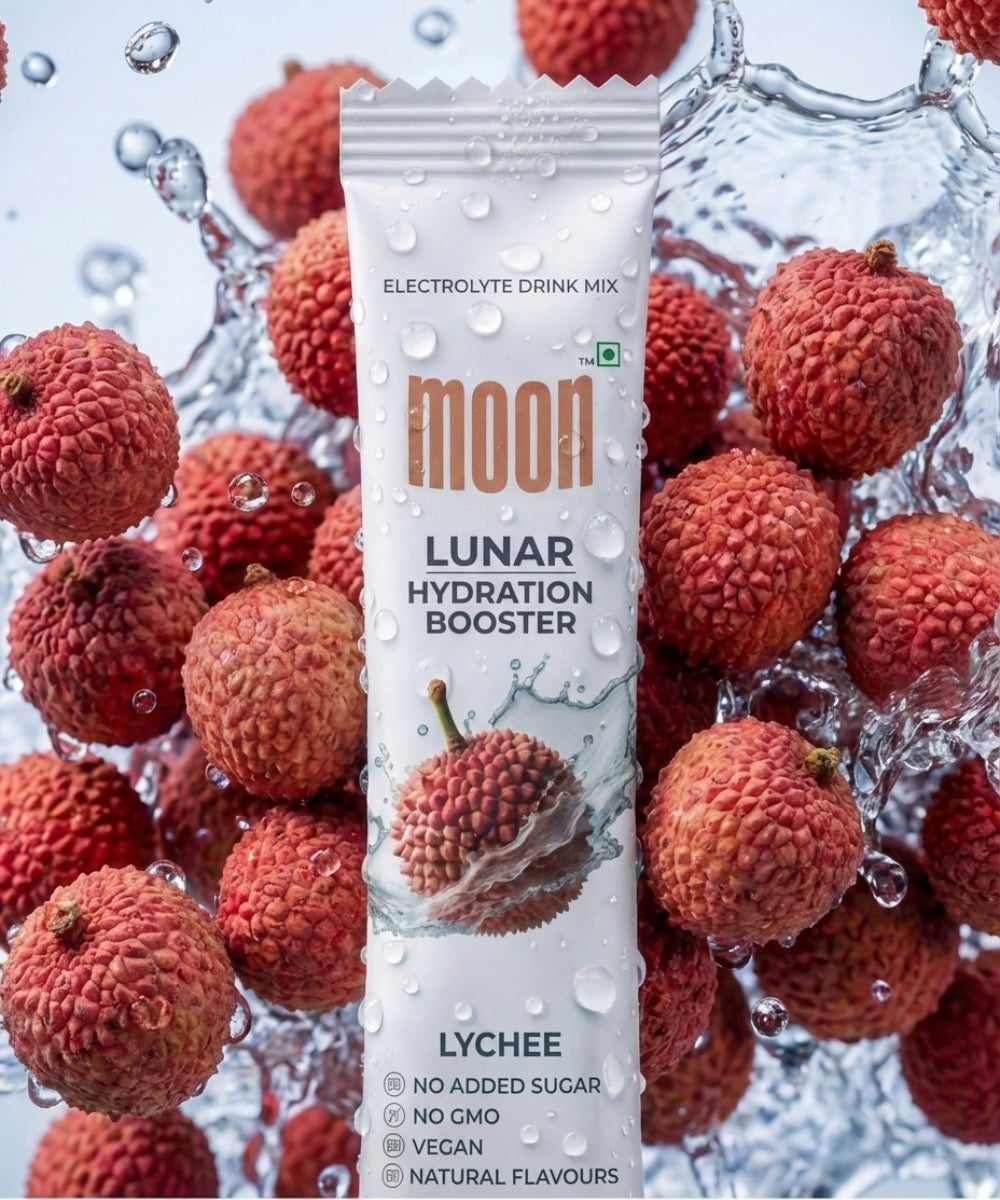 A packet of MOONFREEZE FOODS PRIVATE LIMITED Lunar Hydration Booster - Lychee Flavour, an electrolyte drink with B vitamins, is shown among fresh lychees and water splashes. The pack states no added sugar, non-GMO, vegan, and natural flavors.